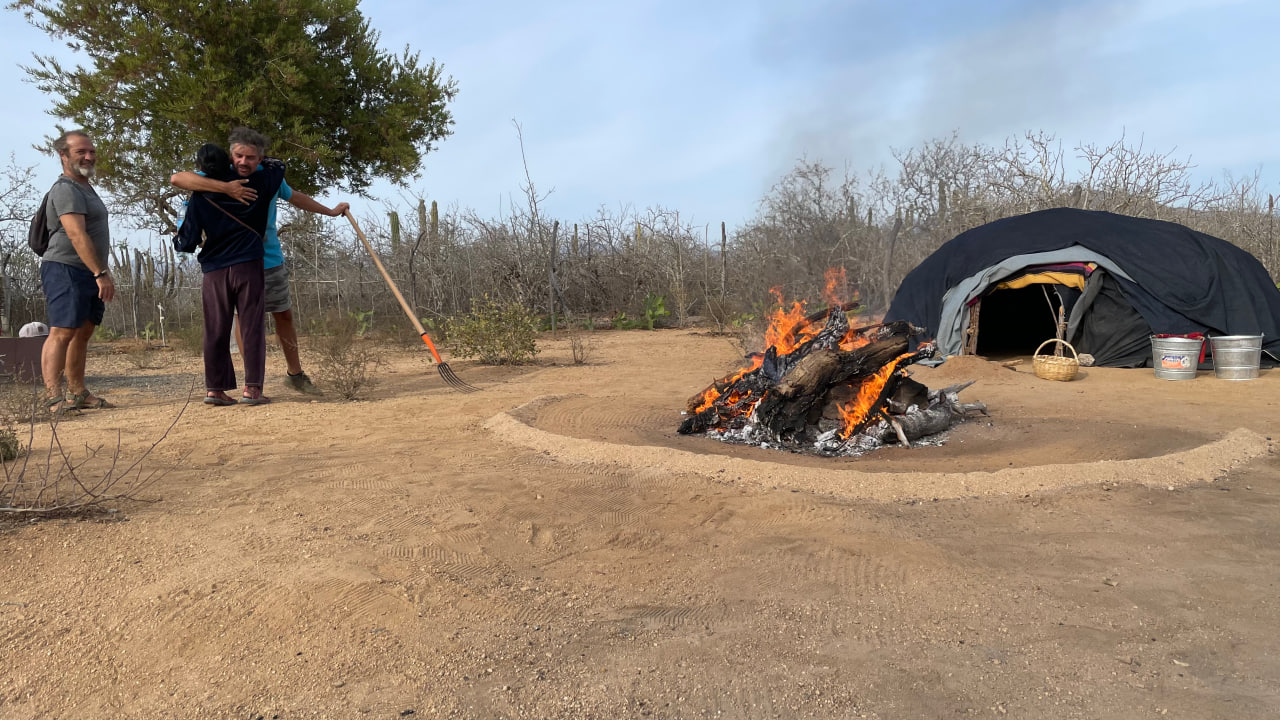 Eine Schwitzhütte mit offenem Eingang und brennender Feuerstelle im Freien